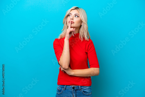 Young Russian woman isolated on blue background showing a sign of silence gesture putting finger in mouth