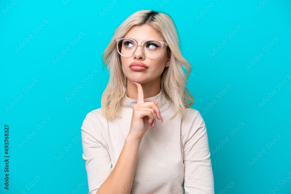 Young Russian woman isolated on blue background With glasses and looking up Young Russian woman isolated on blue background With glasses and looking up