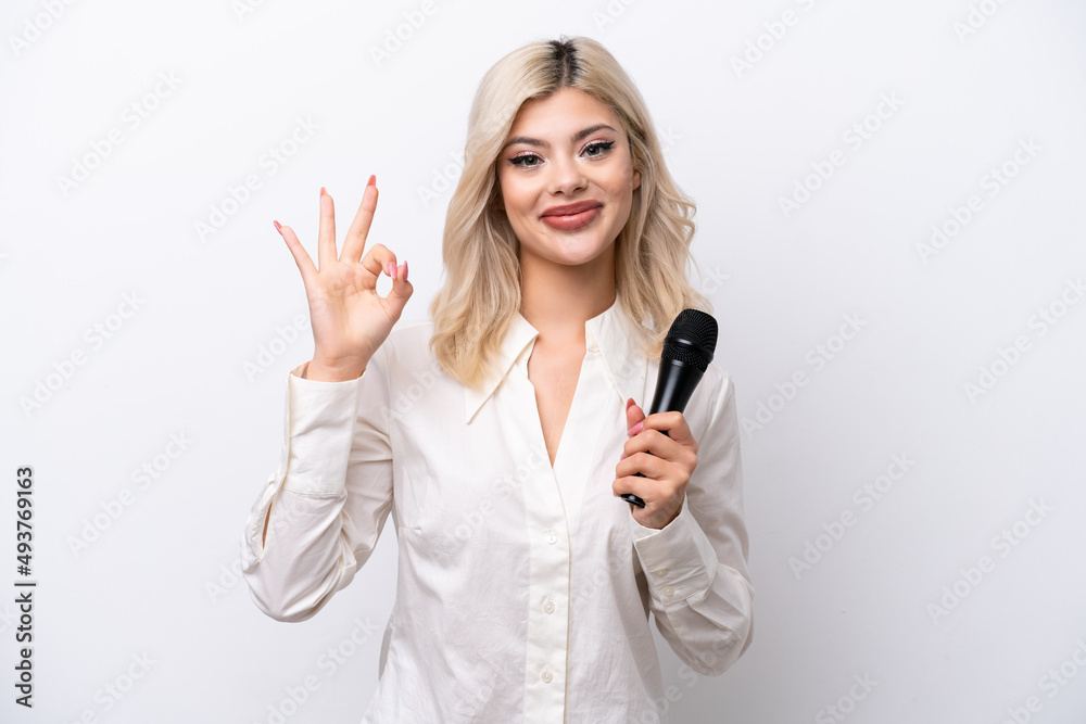 Young singer woman picking up a microphone isolated on white background showing ok sign with fingers Young singer woman picking up a microphone isolated on white background showing ok sign with fingers