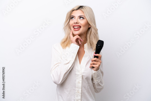 Young singer woman picking up a microphone isolated on white background thinking an idea while looking up