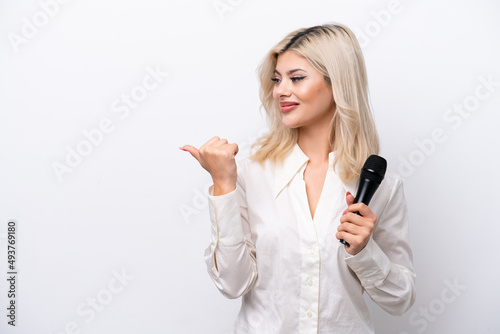 Young singer woman picking up a microphone isolated on white background pointing to the side to present a product