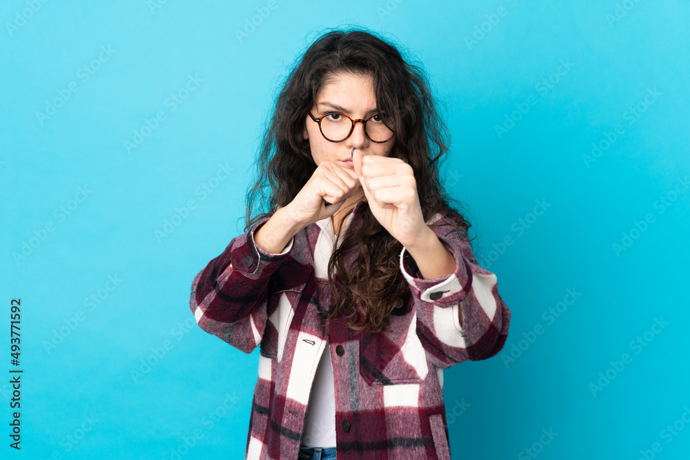 Teenager Russian girl isolated on blue background with fighting gesture Teenager Russian girl isolated on blue background with fighting gesture