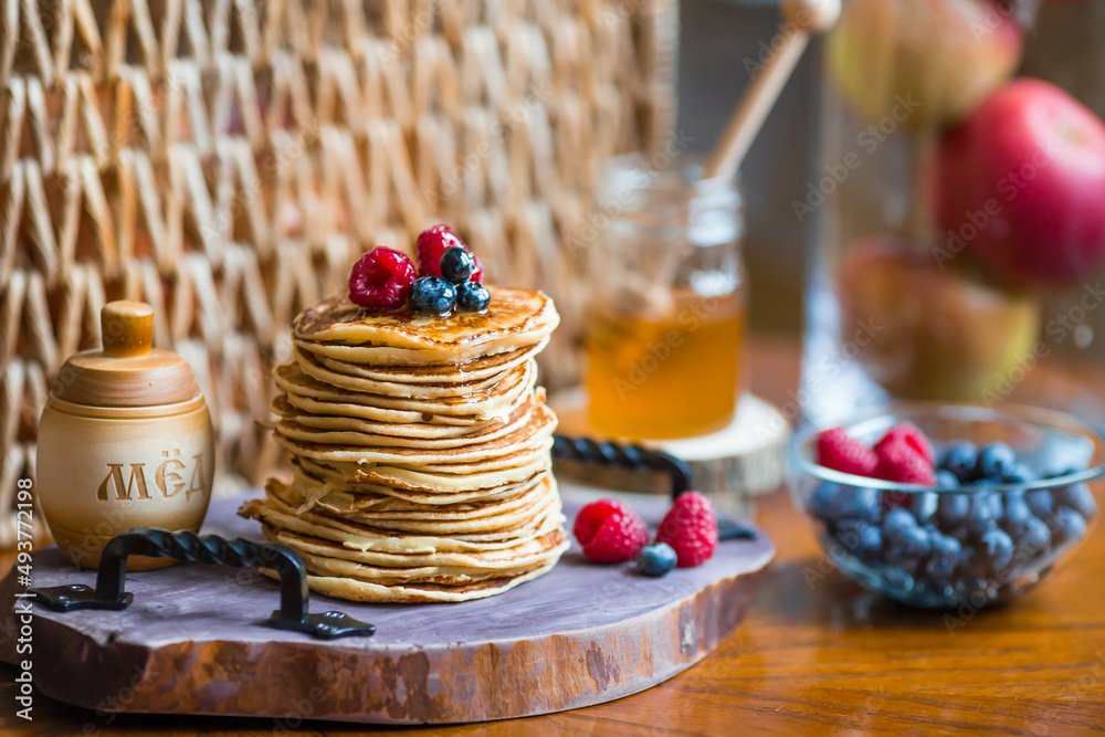 Delicious pancakes with honey, blueberries and raspberries. Next to it is a wooden barrel with an inscription in Russian: Delicious pancakes with honey, blueberries and raspberries. Next to it is a wooden barrel with an inscription in Russian:
