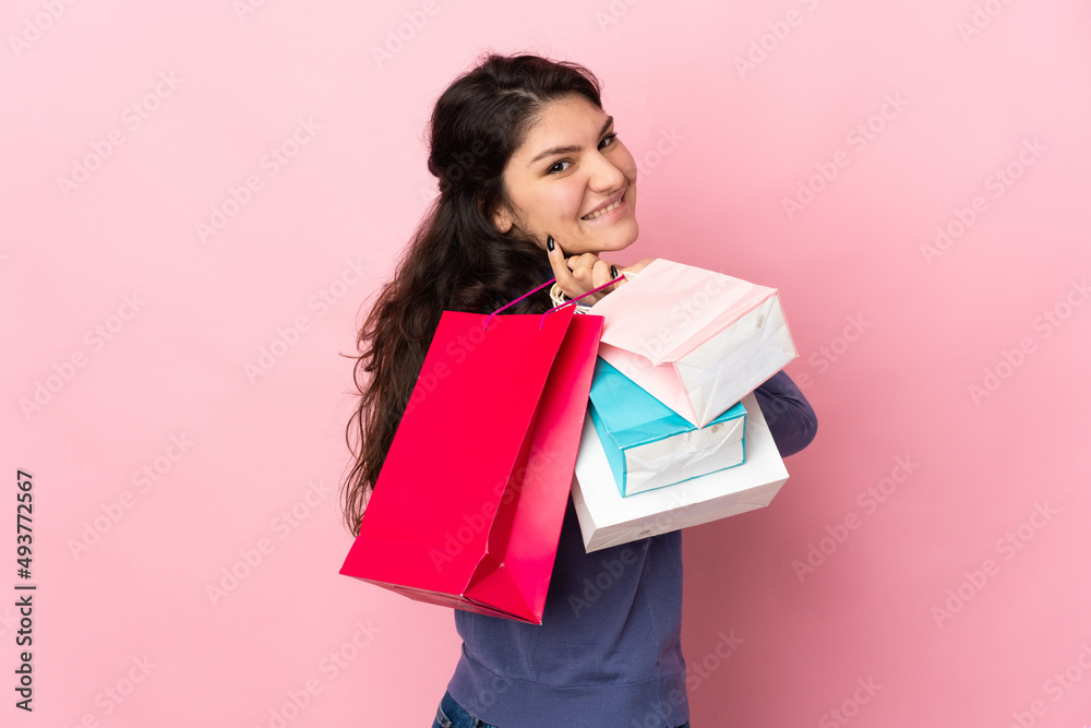 Teenager Russian girl isolated on pink background holding shopping bags and smiling Teenager Russian girl isolated on pink background holding shopping bags and smiling