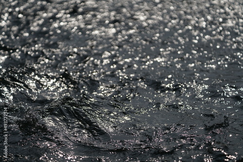 Fließendes Wasser in einem Fluss und mit Sonnenlicht, welches sich im Wasser spiegelt und reflektiert © darknightsky