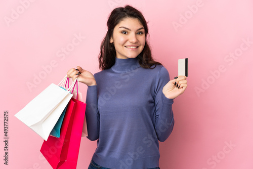 Teenager Russian girl isolated on pink background holding shopping bags and a credit card