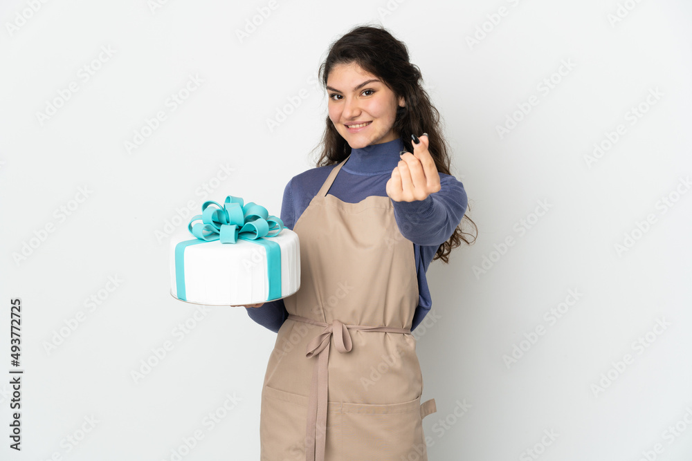 Pastry Russian chef holding a big cake isolated on white background making money gesture Pastry Russian chef holding a big cake isolated on white background making money gesture