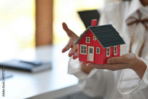 Close up woman's hands holding a red house model, for housing, finance and real estate business.