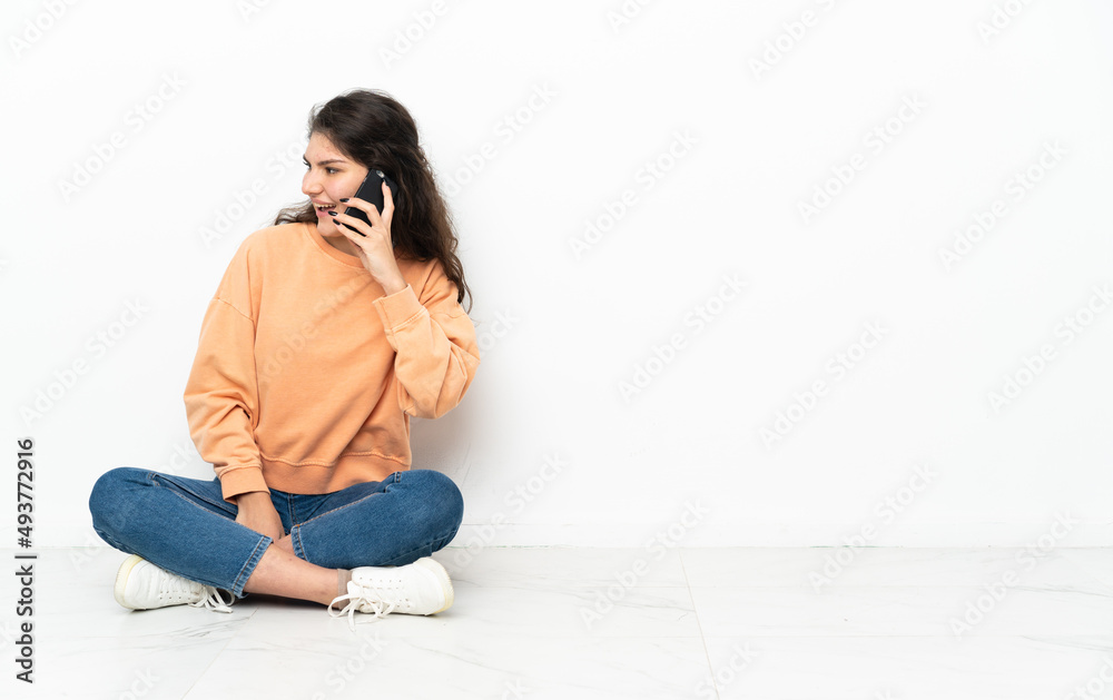 Teenager Russian girl sitting on the floor keeping a conversation with the mobile phone with someone Teenager Russian girl sitting on the floor keeping a conversation with the mobile phone with someone