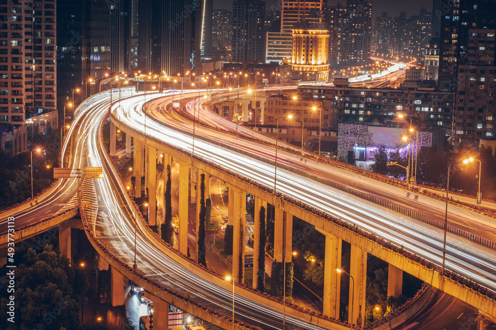 Fototapeta premium Urban overpasses with lights on at night and the urban background in the distance