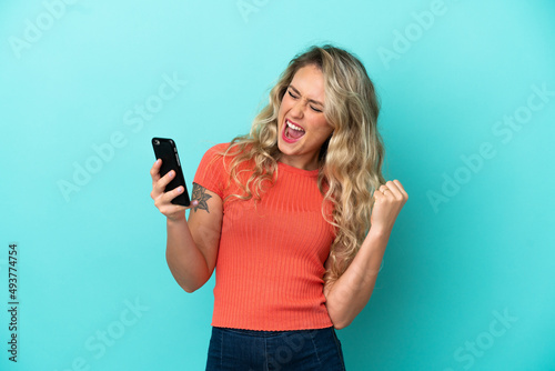 Young Brazilian woman isolated on blue background with phone in victory position