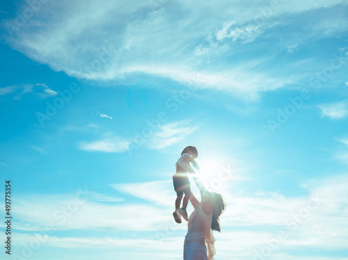 Mother playing with baby boy,mom raises the child in her arms up with blue sky.