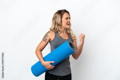 Young sport Brazilian woman going to yoga classes while holding a mat isolated on white background celebrating a victory