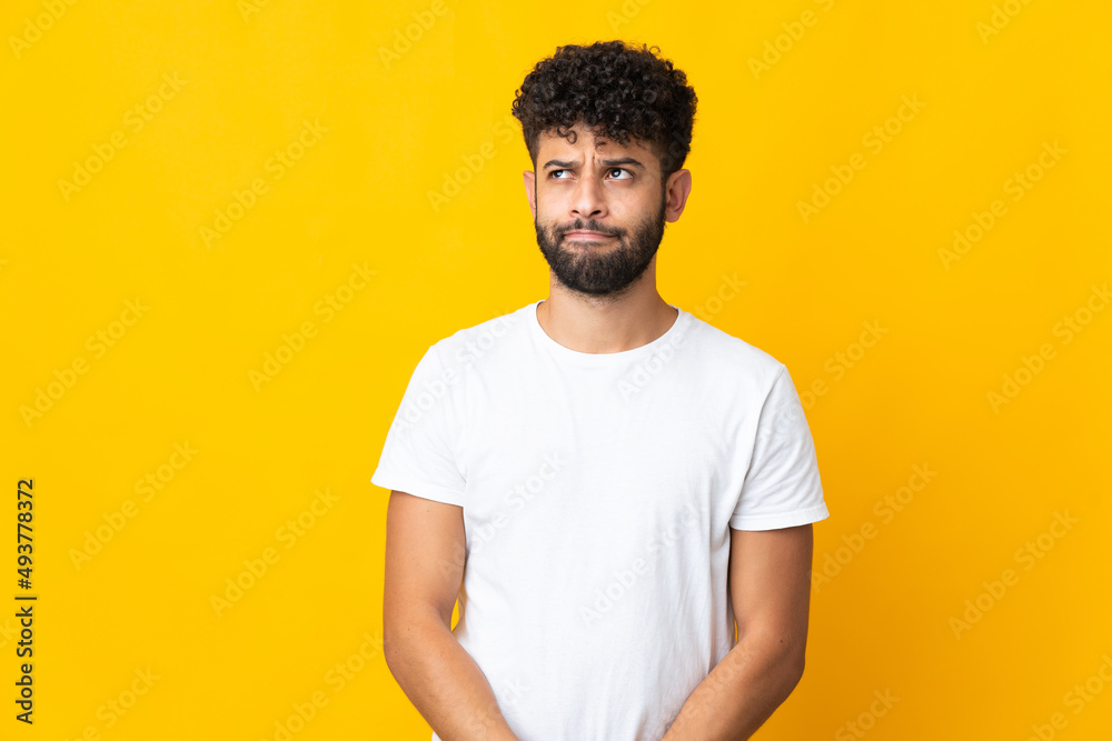 Young Moroccan man isolated on yellow background having doubts while looking up Young Moroccan man isolated on yellow background having doubts while looking up
