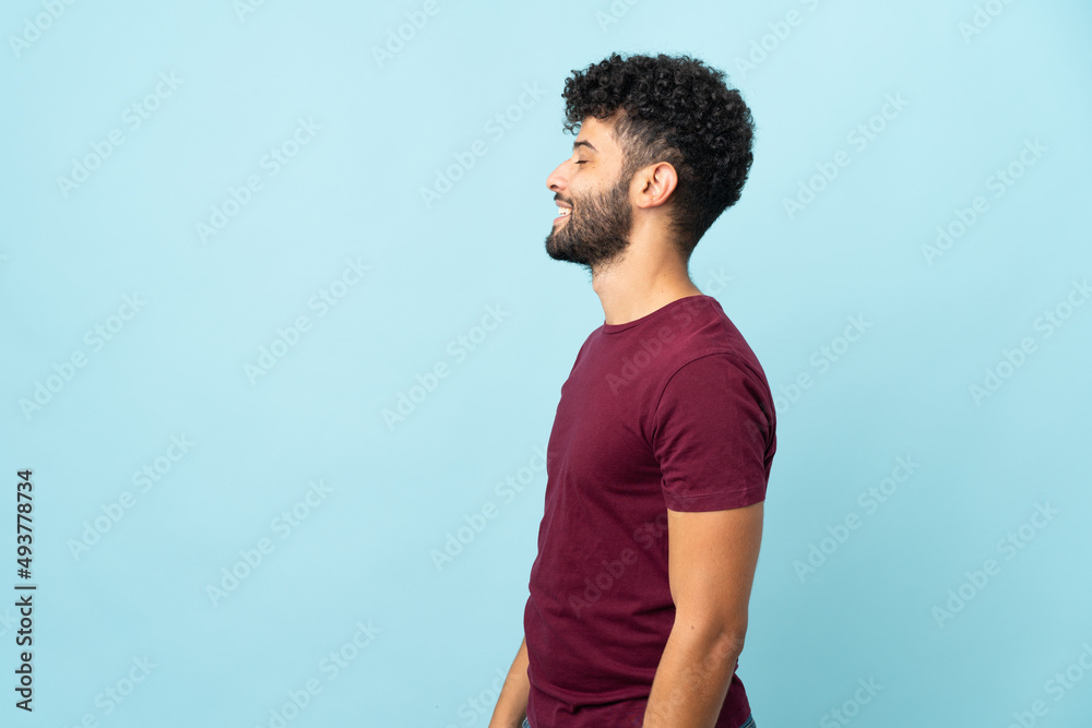 Young Moroccan man isolated on blue background laughing in lateral position Young Moroccan man isolated on blue background laughing in lateral position