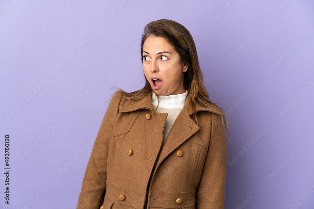 Middle age Brazilian woman isolated on purple background doing surprise gesture while looking to the side Middle age Brazilian woman isolated on purple background doing surprise gesture while looking to the side