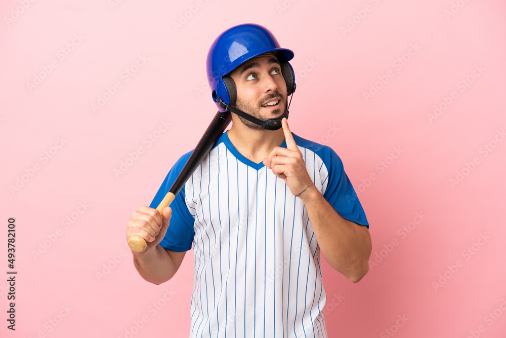 Baseball player with helmet and bat isolated on pink background thinking an idea while looking up Baseball player with helmet and bat isolated on pink background thinking an idea while looking up