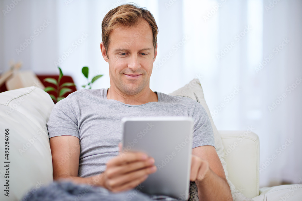 Hes got everything he needs for some serious chilling. Shot of a handsome man relaxing with his tablet at home.