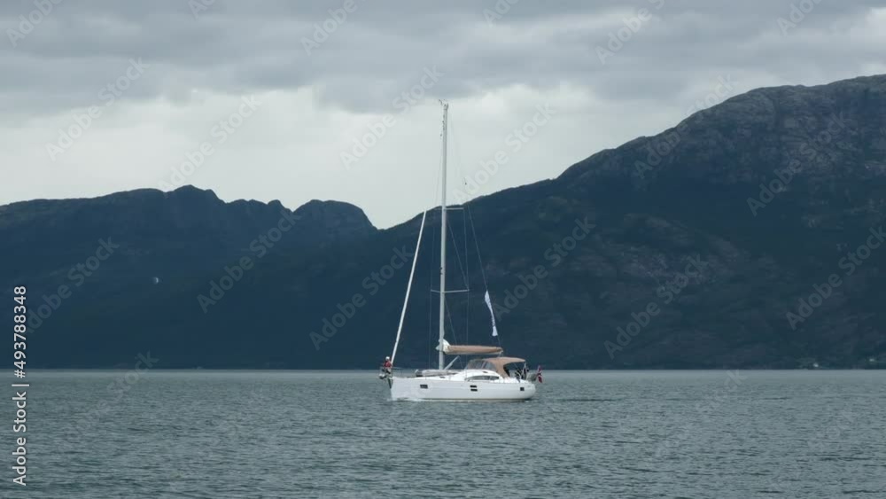 A yacht with lowered sails sails against the background of dark mountains A yacht with lowered sails sails against the background of dark mountains
