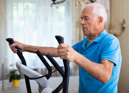 Positive senior man works out on an elliptical machine at home