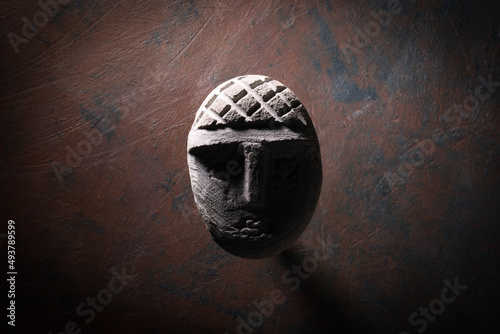 Scultura raffigurante una piccola testa scolpita in un sasso, isolata su fondo scuro
 photo