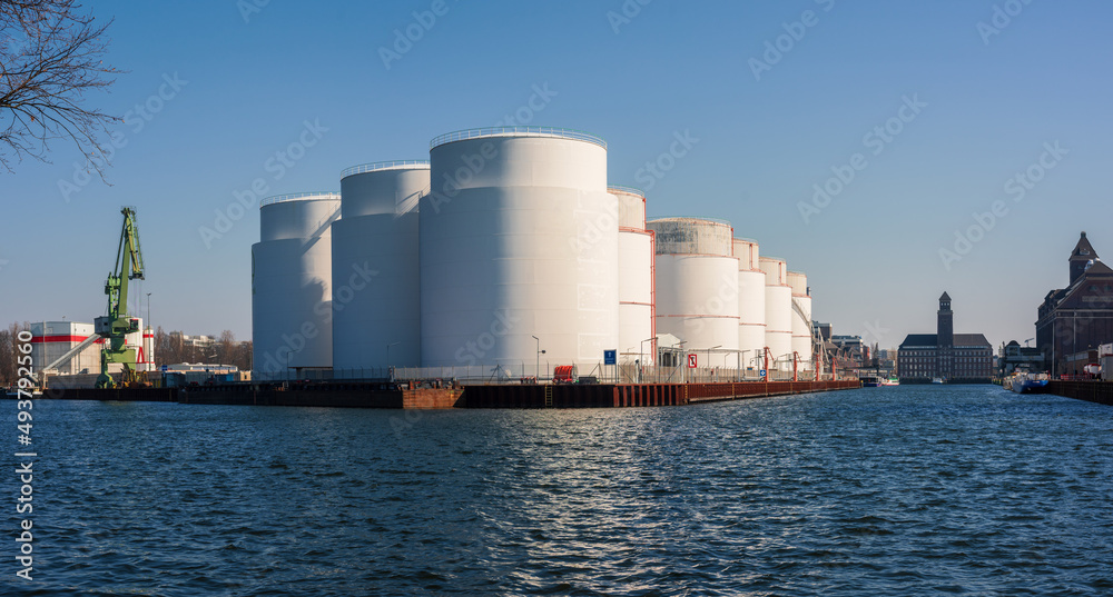 Oil supply. large white steel reservoirs of a tank farm for mineral oil at a canal. Oil supply. large white steel reservoirs of a tank farm for mineral oil at a canal.