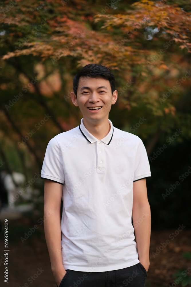 one Asian young man smiling looking at camera with blur maple tree  