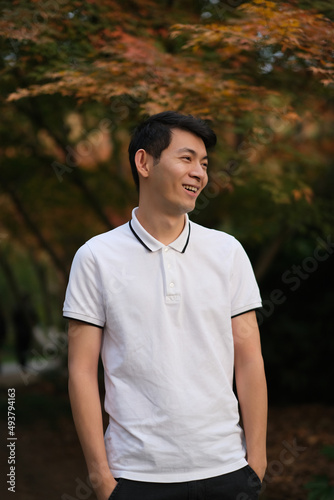 one handsome Asian young man smiling and looking away with blur maple tree 