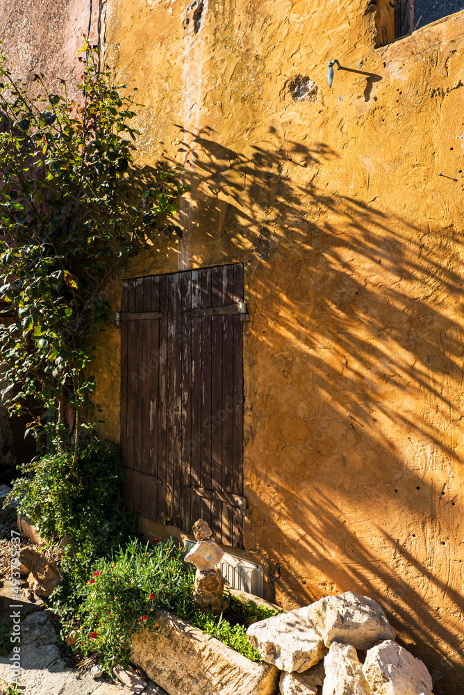 Yellow colored wall and red wooden window shutter at the famous french Roussillon village.