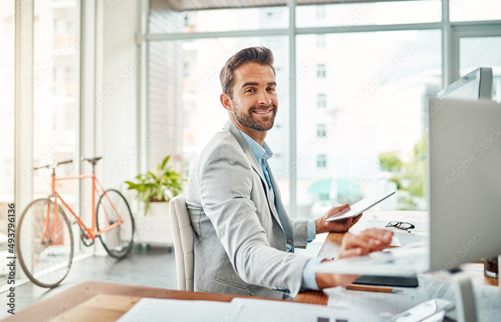 Multitasking my way to success. Portrait of a handsome young businessman working on a laptop and digital tablet in an office. Multitasking my way to success. Portrait of a handsome young businessman working on a laptop and digital tablet in an office.