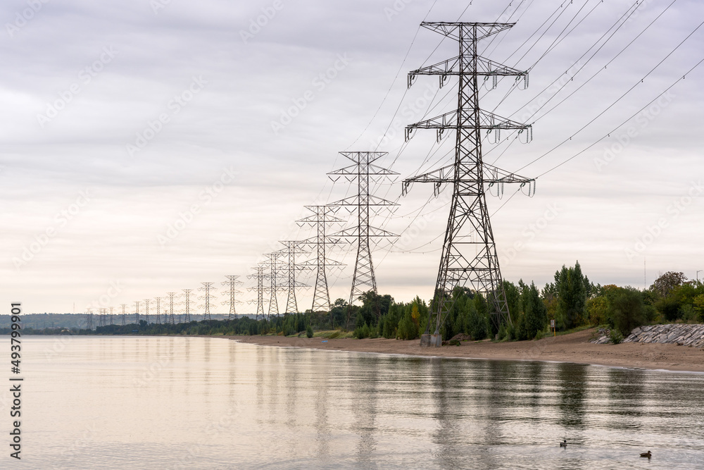 Tall high voltage electricity pylons on the shore of a lake on a cloudy autumn day
