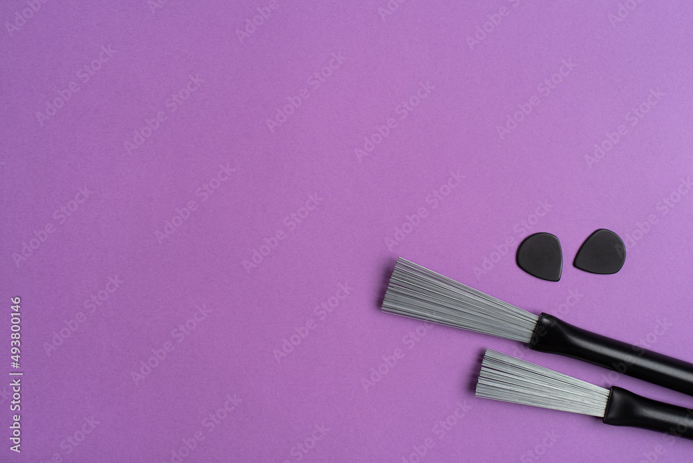Drum brushes and guitar picks on a purple background. Flat lay, top view. Drum brushes and guitar picks on a purple background. Flat lay, top view.