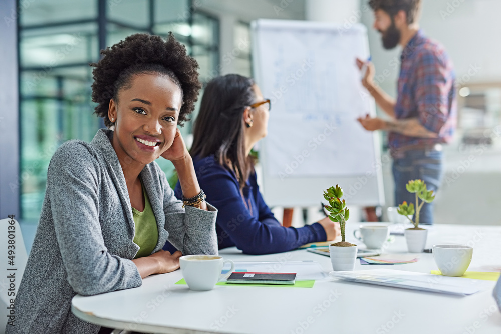 Dont stop until youre proud. Portrait of a young businesswoman sitting in a meeting with colleagues in the background. Dont stop until youre proud. Portrait of a young businesswoman sitting in a meeting with colleagues in the background.