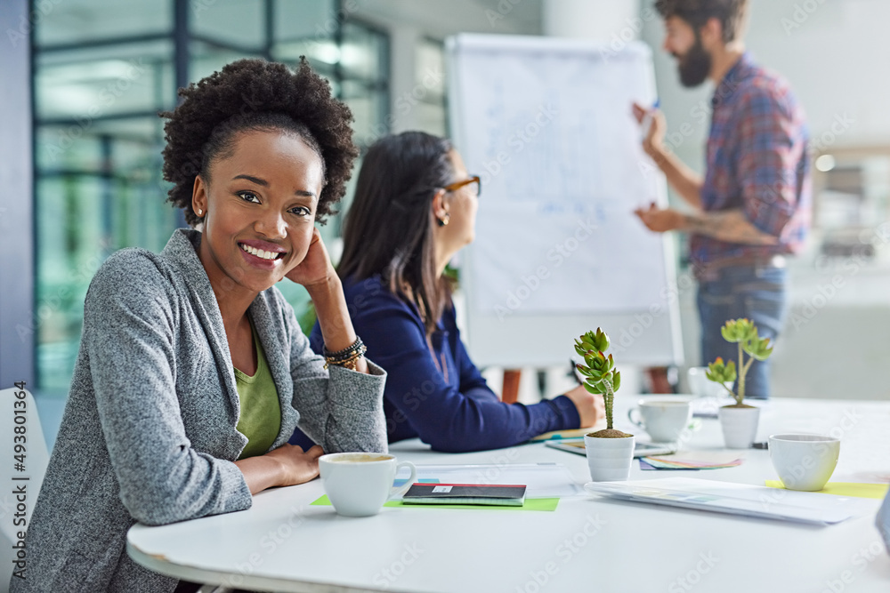 Dont stop until youre proud. Portrait of a young businesswoman sitting in a meeting with colleagues in the background.