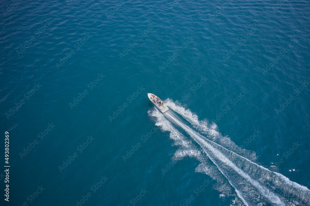 Modern boat in motion making a trail on the water top view. Boat moving fast aerial view. One boat on blue water drone view.