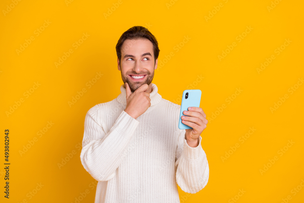 Photo of intelligent guy hold telephone finger chin look empty space wear white sweater isolated yellow color background Photo of intelligent guy hold telephone finger chin look empty space wear white sweater isolated yellow color background
