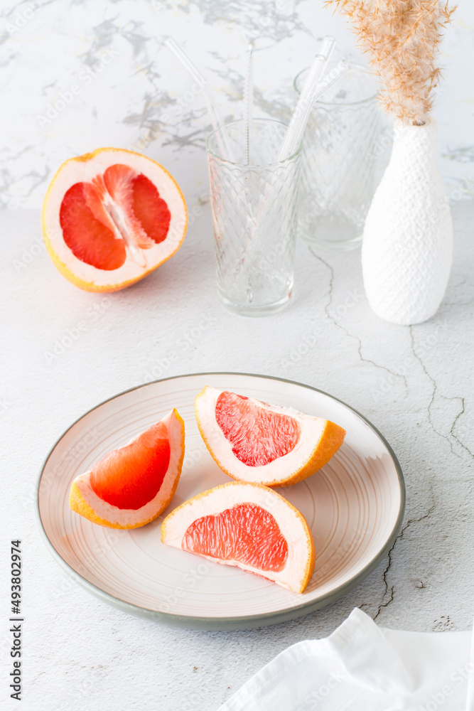 Pieces of juicy fresh grapefruit on a plate on a light table. Vitamin diet food. Vertical view Pieces of juicy fresh grapefruit on a plate on a light table. Vitamin diet food. Vertical view