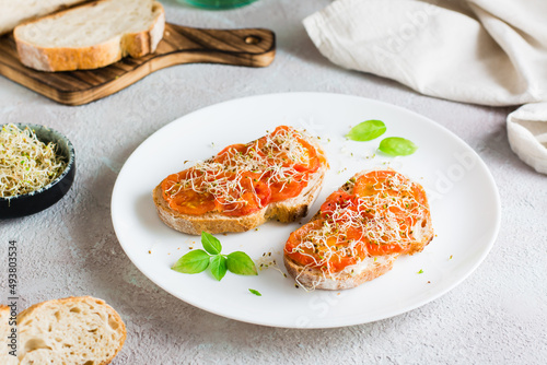Appetizing sandwich with sun-dried tomatoes and clover and alfalfa sprouts on a plate on the table. Diet organic food