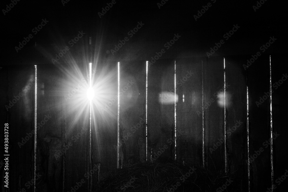 Obraz premium lights shining through wooden stable wall