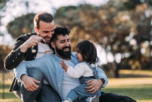 Male gay family hugging and playing with their little daughter in the park. © antoniosantosc