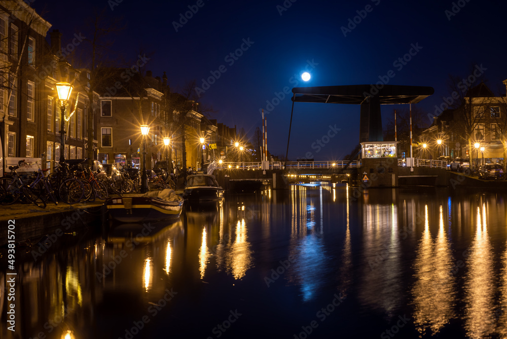 Leiden, The Netherlands, March 18, 2022, night view of the canal with historic houses and small boats and full moon