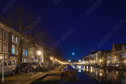 Leiden, The Netherlands, March 18, 2022, night view of the canal with historic houses and small boats and full moon © zivko.trikic