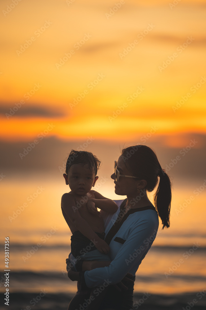 Happy family resting at beach in summer, Mother and baby boy feet at the sea foam at the sunlight water is moving