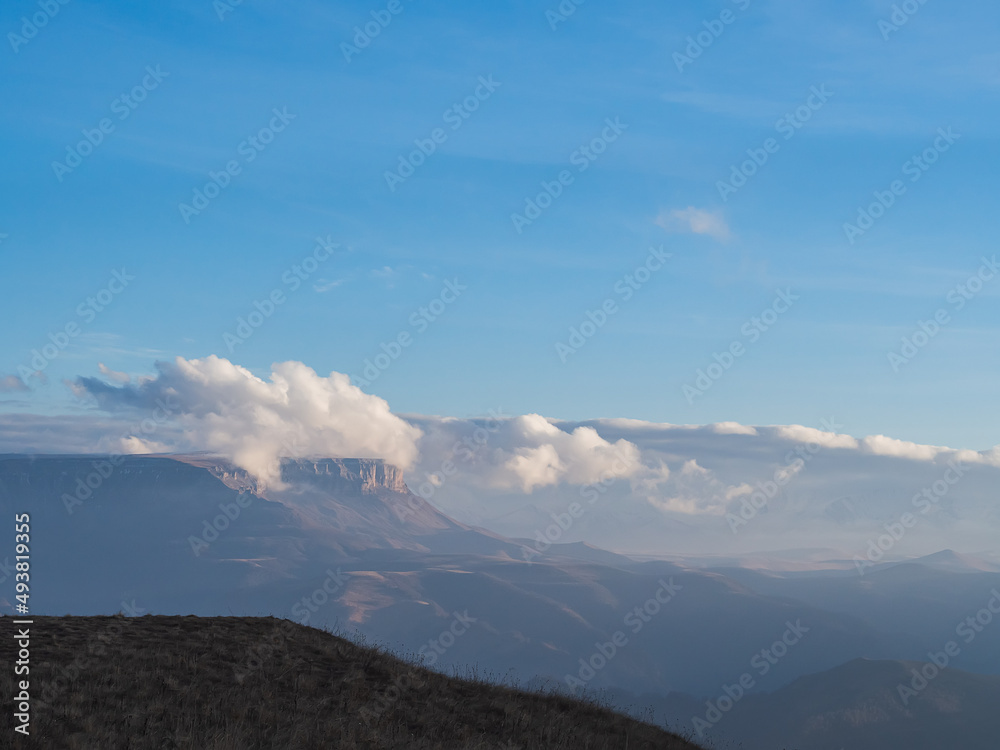 Hiding in the clouds under a bright blue sky is the Bermamyt plateau surrounded by a mountain valley on an autumn day Hiding in the clouds under a bright blue sky is the Bermamyt plateau surrounded by a mountain valley on an autumn day
