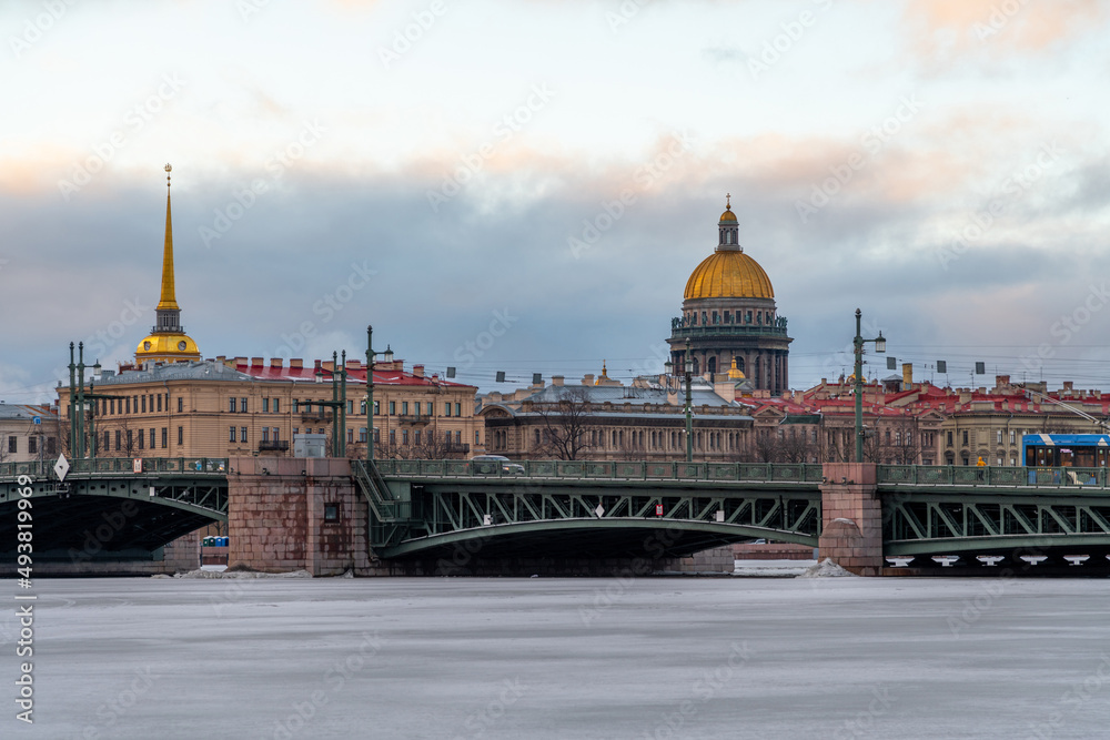 Winter cityscape of Saint Petersburg city, Russia. Palace bridge above Neva river covered with ice. Saint Isaac's Cathedral and Admiralty Building in the background. Travel in Russia theme.