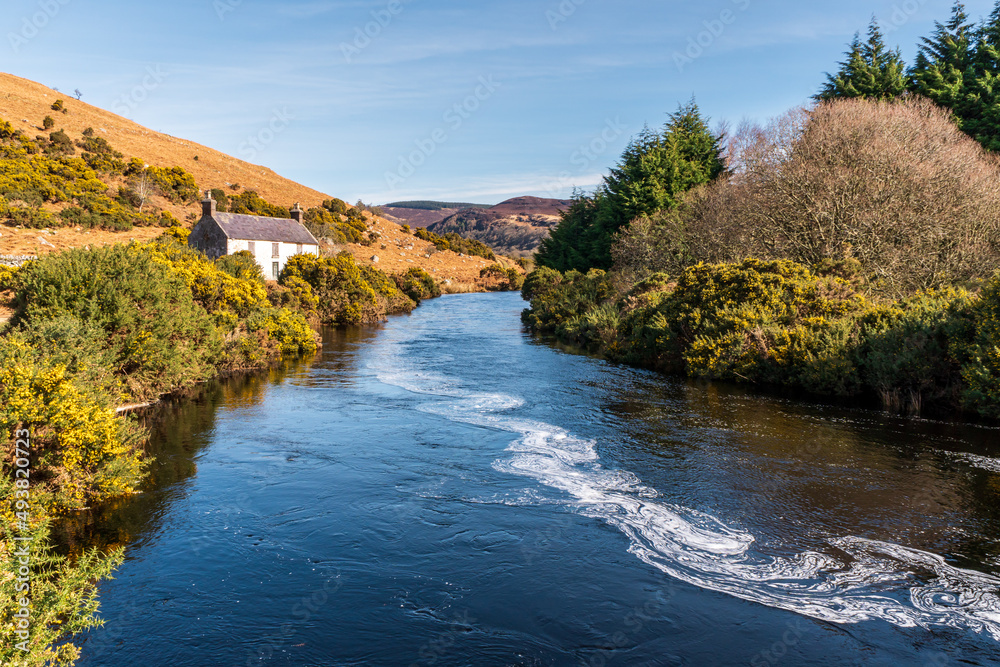 River passing near an old Irish cottage in a beautiful spring scenery. Mountain rustic landscape.