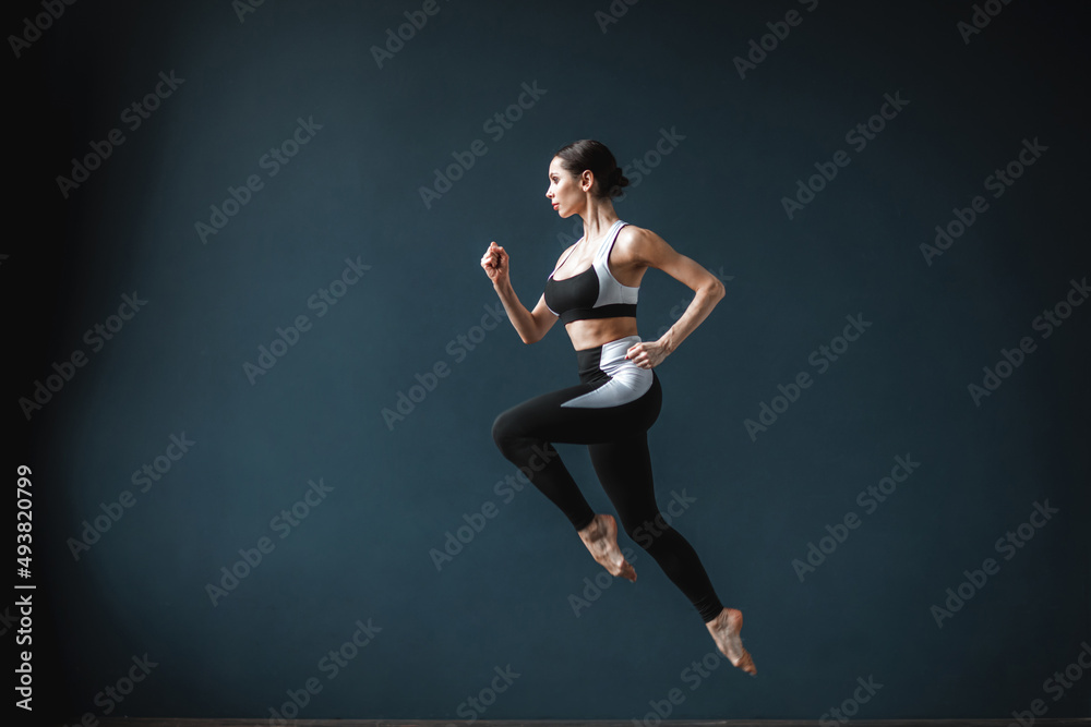Beautiful fitness woman in a jump full length over gray