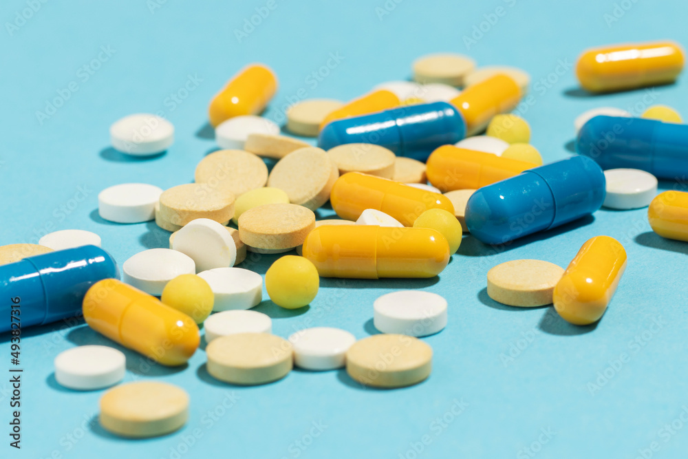 Different colored pills and capsules scattered on a blue background.