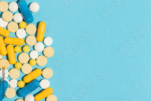 Different colored pills and capsules scattered on a blue background. Top view with copy space.