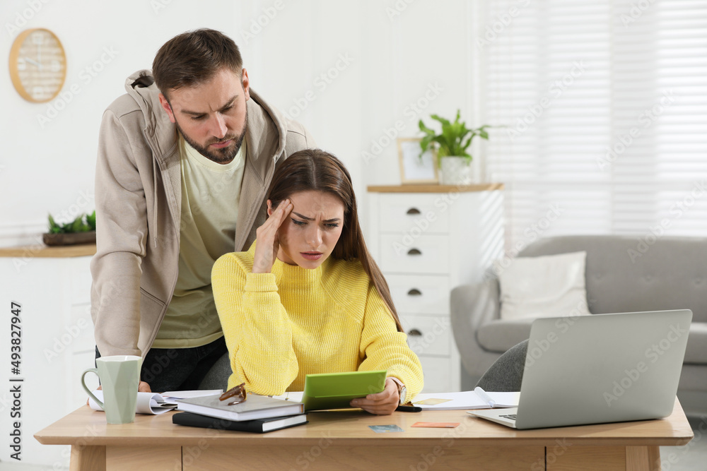 Young couple discussing family budget at table in living room Young couple discussing family budget at table in living room